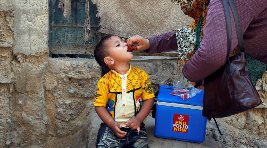 Pakistani health worker giving polio vaccine drops to a child during a vaccination drive.